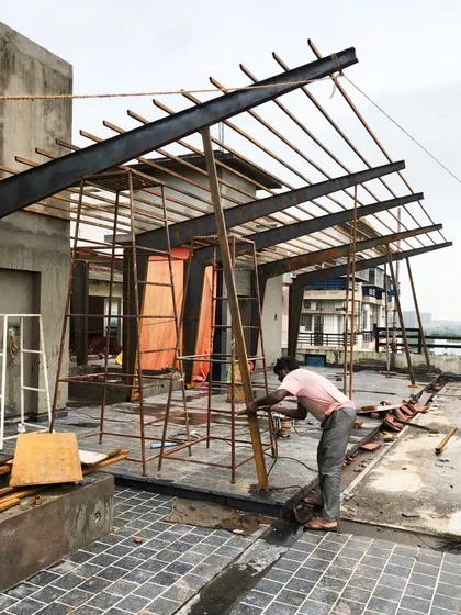 A work-in-progress shot of a steel roof structure being fabricated on a terrace. The image captures the raw energy of construction and the skeletal beauty of the steel frame before it is completed, showing the geometry that underpins the final form.