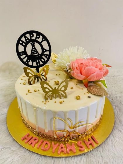 A simple yet elegant butterfly cake with a white drip, topped with a pink flower and golden butterflies.