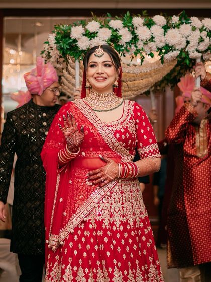 The bride's happy entrance under the phoolon ki chadar, waving to her loved ones. Her radiant smile lights up the entire frame.