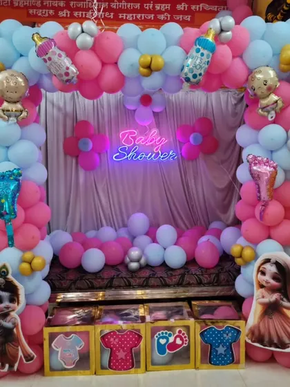 A cozy baby shower setup for a home celebration. We decorated the seating area with a pink and blue balloon frame, a 'Baby Shower' neon sign, and cute character props.