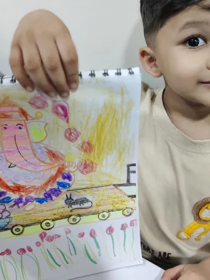 An adorable young boy shows off his imaginative drawing of Lord Ganesha. His unique creation features a cart, a bowl of colourful ladoos, and a garden of tulips, a perfect example of the boundless creativity I encourage in my kids' art classes.