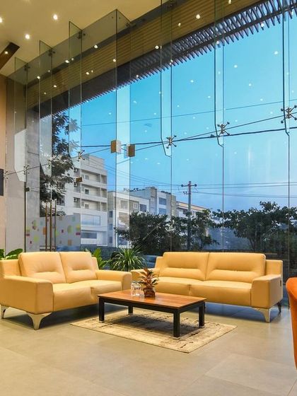 The reception and lounge area of a commercial showroom, featuring a double-height glass facade that fills the space with natural light. The design is open, modern, and welcoming.