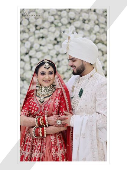 A happy, smiling couple portrait against a beautiful floral backdrop. The bride's makeup looks fresh and radiant.