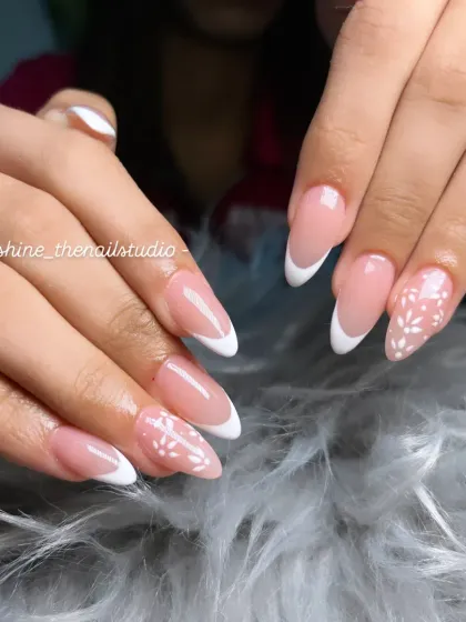 A clean and classic white French manicure on almond-shaped nails, with a delicate hand-painted white floral pattern on the accent nails.