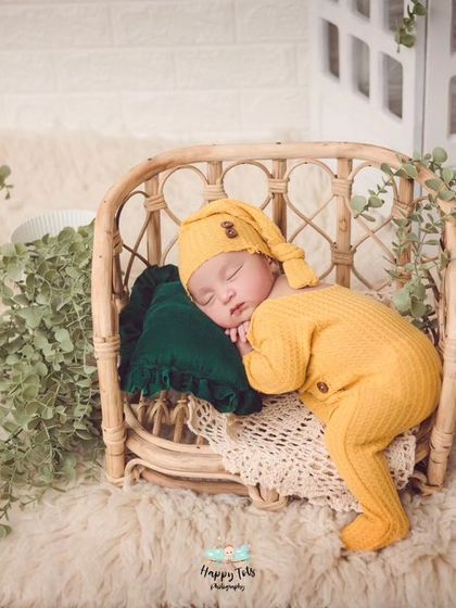 The perfect little bundle. This baby is posed in a yellow knit outfit on a miniature rattan bed, surrounded by greenery for a natural feel.