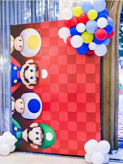 A fun Super Mario themed backdrop featuring Mario, Luigi, and Toad peeking out from the side. The red checkerboard pattern and balloon cluster add to the playful, game-inspired vibe.