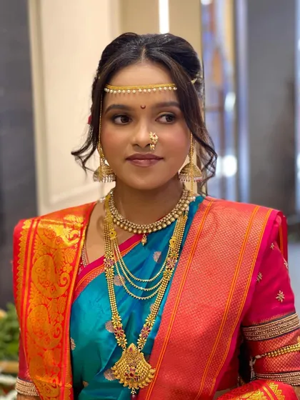 A beautiful Maharashtrian bride in a blue and pink Paithani saree. The makeup is soft and radiant, with a traditional updo and mundavalya completing the look.