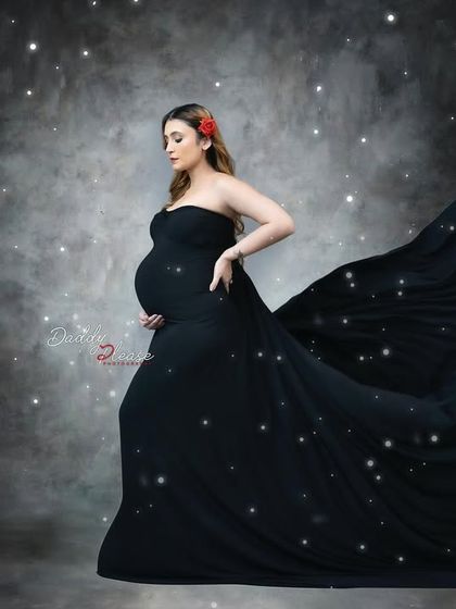 A magical and dreamy portrait of an expectant mother in a black gown with a long, flowing train. The added sparkle effect creates a celestial, starry night feel.
