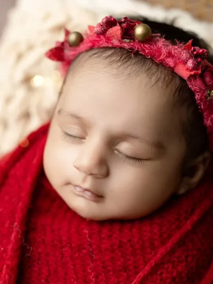 A close-up of a newborn in our Christmas setup, with a festive red headband and twinkling lights in the background.