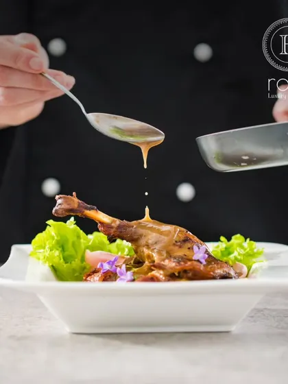 A chef carefully drizzles sauce over a lamb shank. This action shot captures the final, artistic touch that elevates a dish from simple food to a gourmet experience.