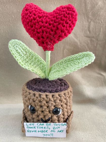 This adorable crochet pot features a bright red heart flower and a sweet face. It holds a tiny customizable note, making it a truly personal and encouraging gift for a friend or loved one.