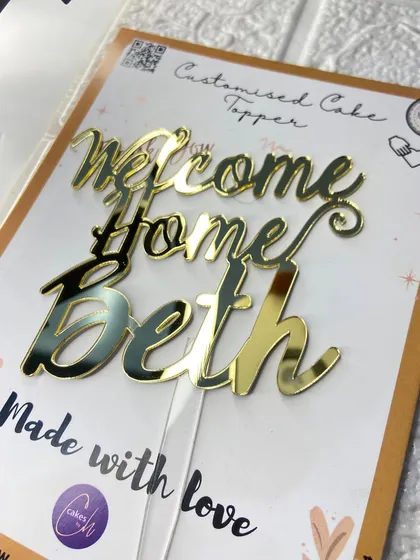 The "Welcome Home Beth" topper in its packaging, ready to be part of a happy reunion.