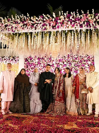 A perfect family portrait. The couple stands with their loved ones on the grand floral stage, a beautiful memory of togetherness from their special day.