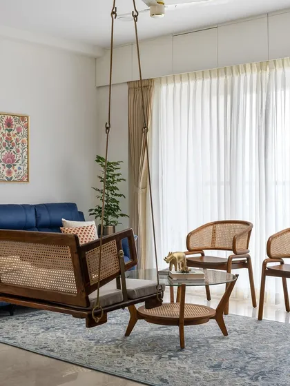 Another view of the 'Malhar' living room, highlighting the custom wooden swing with cane weaving, paired with matching chairs and a glass-topped coffee table.