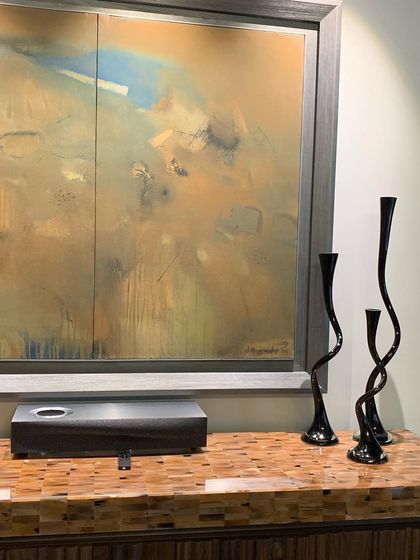 A console with a top made of inlaid wood pieces, creating a beautiful, textured surface. Above it, an abstract landscape painting and sculptural vases complete the vignette.