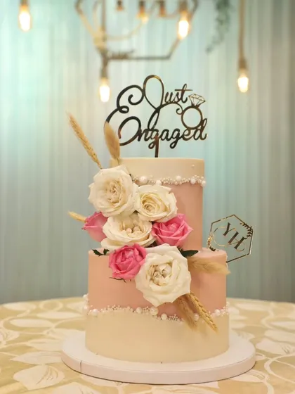 A lovely two-tier engagement cake in shades of pink and white, adorned with a cascade of roses.