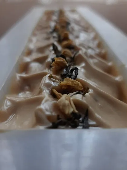 A close-up of my Earl Grey Tea soap, freshly poured. The top is textured and decorated with tea leaves and jasmine buds, capturing the essence of a warm cup of tea.