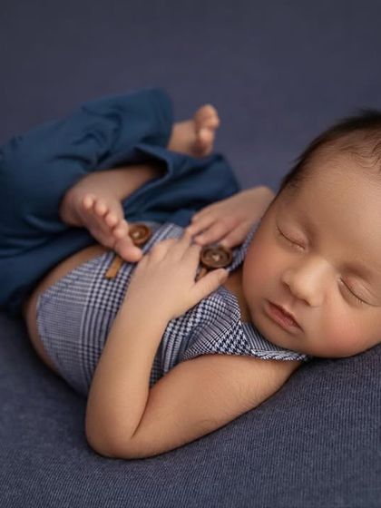 A dapper little man in a plaid and blue outfit, sleeping peacefully on a blue backdrop.