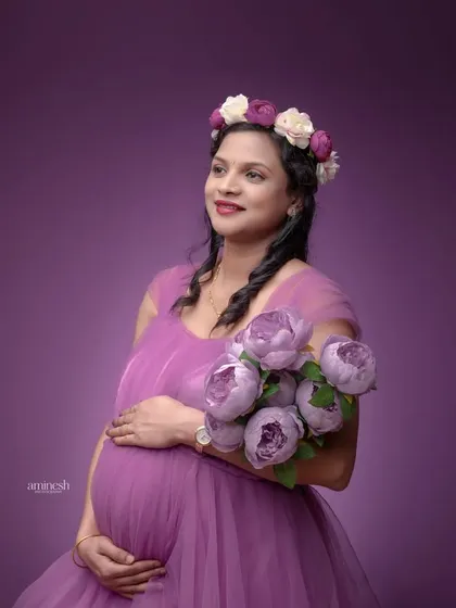 A lovely portrait against a solid purple backdrop, matching the tones in the gown. The floral crown and bouquet tie the whole look together, creating a cohesive and beautiful image.