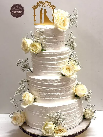 Simple elegance is timeless. This four-tiered wedding cake is finished with textured whipped cream and adorned with fresh white roses and baby's breath, proving that a classic design can be the most beautiful centerpiece for your special day.
