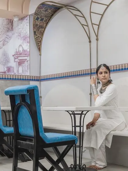 The seating area continues the architectural theme. The custom chairs feature a backrest inspired by traditional arches, and the delicate metal frames above the seating echo the filigree work found in historic Indian design.