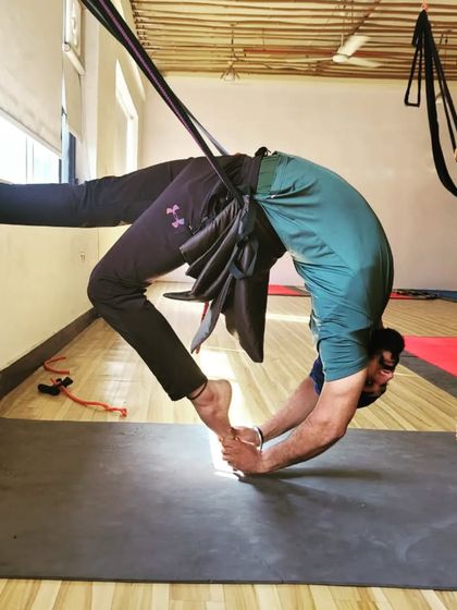 This student is using the wall and a sling to work on grabbing their ankles in a deep backbend, a key step towards mastering more advanced poses.