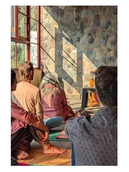 Sunlight streams into the meditation hall, casting shadows across the natural stone wall. This image captures the interplay of light, texture, and human presence that brings the space to life.