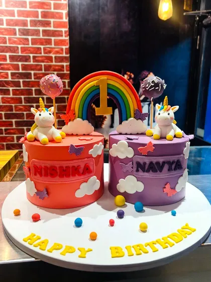 A set of two matching unicorn cakes for twins Nishka and Navya's first birthday, complete with rainbows and fondant clouds.