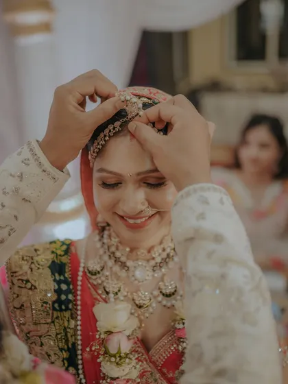 A close-up of a sacred wedding ritual. The groom gently places the maang tikka on the bride's forehead, a moment filled with tradition and love.