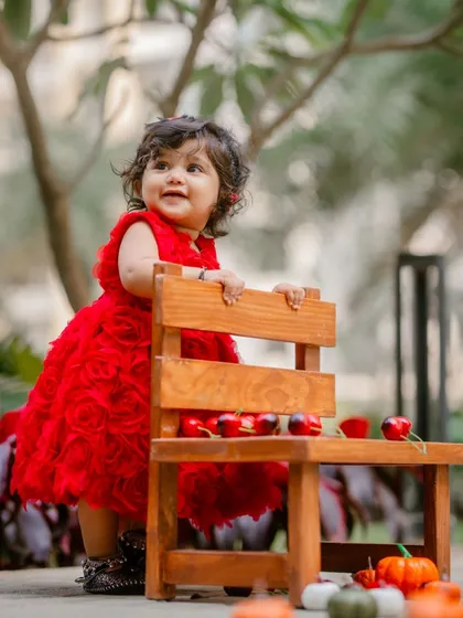 An adorable baby girl in a vibrant red dress for her first birthday shoot. I use simple props like this small wooden chair to add charm without distracting from the star of the show.