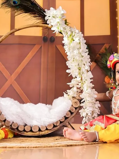 A serene portrait of baby Krishna sitting beside a decorated swing, creating a peaceful and divine atmosphere.