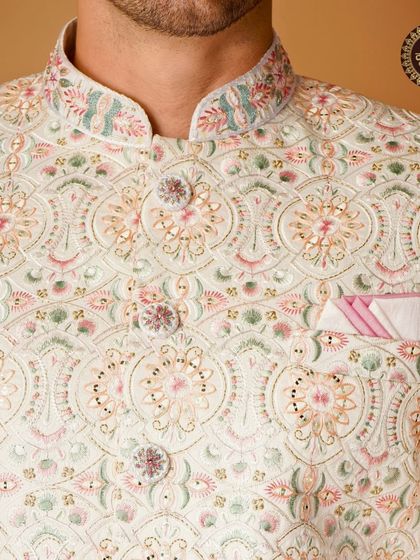 A close-up of a white sherwani with intricate pastel embroidery, highlighting the beautiful threadwork on the collar and placket.