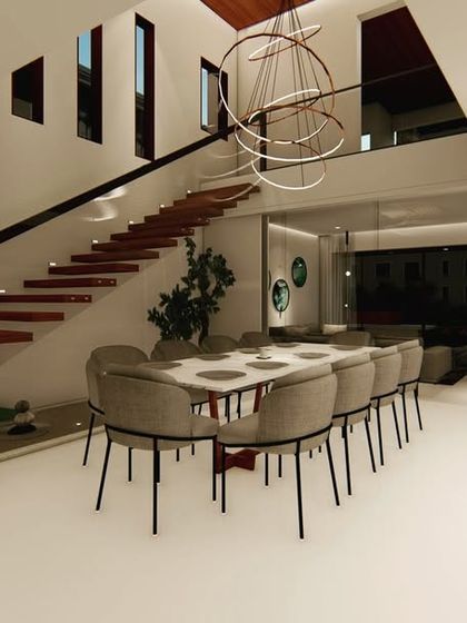 A sophisticated dining area under a floating staircase. The design is minimalist and modern, with grey upholstered chairs and a simple white table, allowing the architectural elements to stand out.