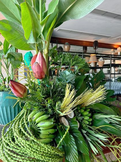 A stunning floral arrangement made with tropical elements like banana flowers, unripe bananas, and lush green leaves.