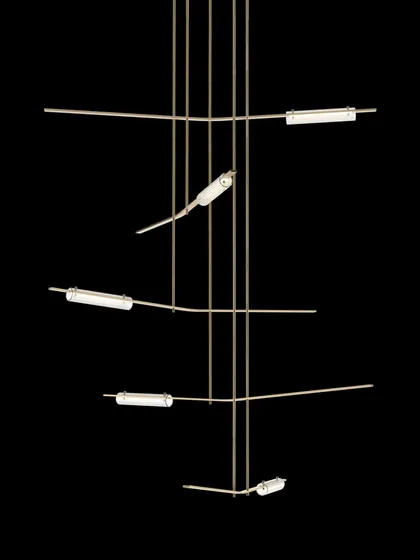 The Volant chandelier by Gabriel Scott, shown against a black background to emphasize its pure, architectural form. The angled, tubular glass elements give the impression of objects in orbit.