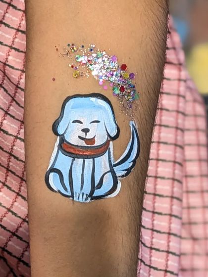 A happy blue dog with a red collar, painted on an arm with a puff of glitter.