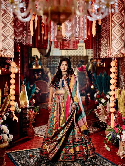 The bride shines in her colorful lehenga, standing in the immersive passageway of hanging rugs and lanterns.