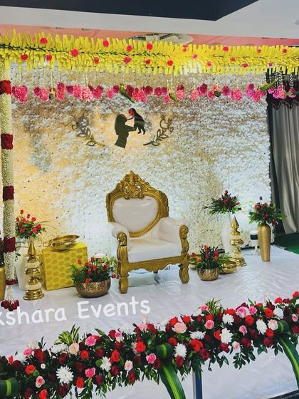 A beautiful Seemantham stage with a backdrop made entirely of fresh white flowers. The design is personalized with a mother and child silhouette and accented with red and pink floral arrangements.