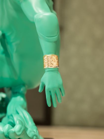 A detail of the "Liberty in Motion" sculpture, focusing on the golden cuff on her wrist, a subtle nod to modern luxury.