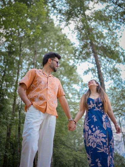 A low-angle shot of a couple holding hands and walking through a forest, making them look majestic among the tall trees.