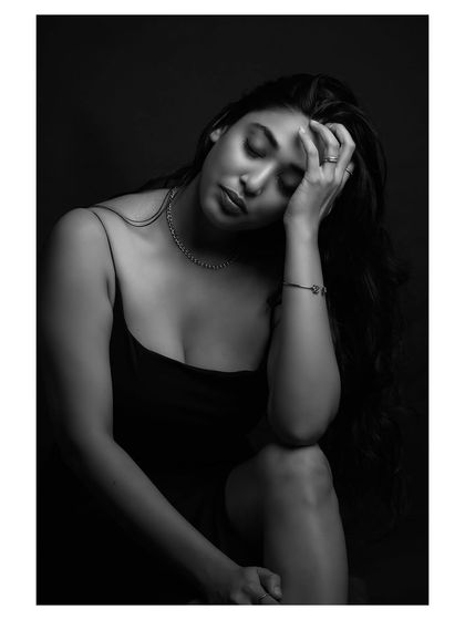 A contemplative black and white portrait. The model's pose and the soft lighting create a sense of quiet introspection and vulnerability.