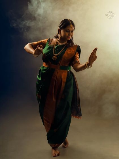 A dynamic portrait of a mom-to-be in a classical dance pose, showcasing grace and strength in a traditional green and orange saree.