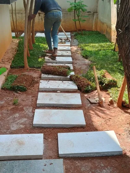 My team member is installing rolls of fresh grass turf around the newly laid stepping stones, carefully fitting them into place.