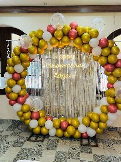 A beautiful and traditional Annaprashan ceremony decoration. The circular balloon arch in gold, white, and rose gold against a shimmering silver curtain creates a festive and sacred space for the baby's first rice-eating ceremony.