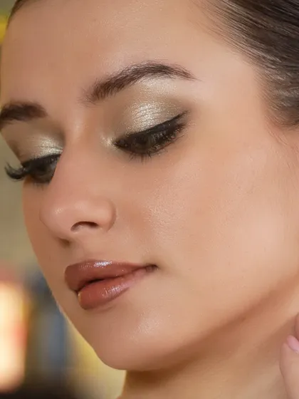 A close-up view of a sophisticated eye makeup application. This look features a metallic champagne eyeshadow with a sharp, winged eyeliner and perfectly sculpted brows, paired with a glossy nude lip for a modern and polished finish.