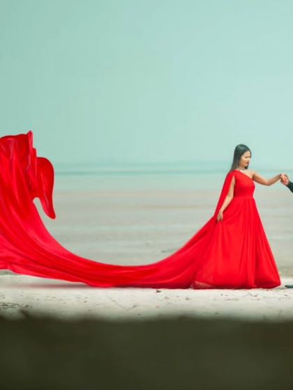 The red trail gown creates a beautiful S-curve on the sand, leading the eye to the romantic couple. This is a simple yet powerful composition for a beach pre-wedding shoot.