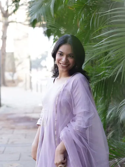 A soft and dreamy portrait, with the model in a lavender Anarkali set against a backdrop of lush palm leaves.