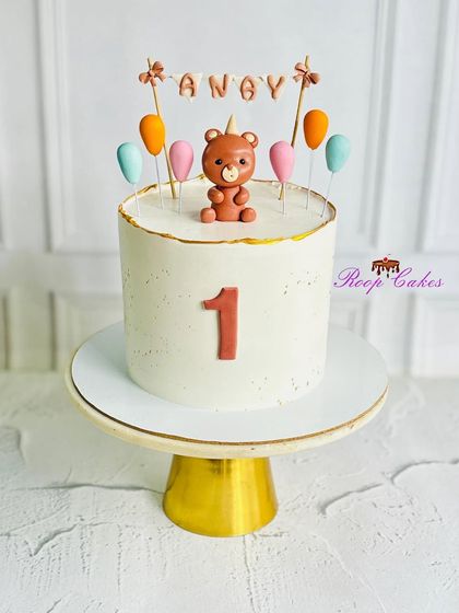A simple and charming teddy bear cake for Anay's first birthday. This tall cake is topped with a small fondant bear and a balloon banner, perfect for a minimalist celebration.