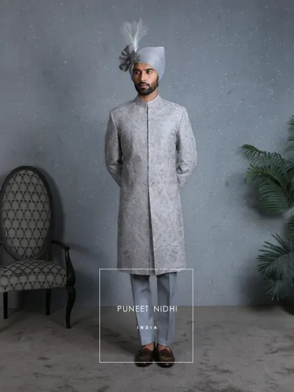 A powder blue wedding sherwani inspired by Mughal architecture, adorned with intricate zari embroidery in silver and gold threads, weaving paisley and floral artistry into every fold.