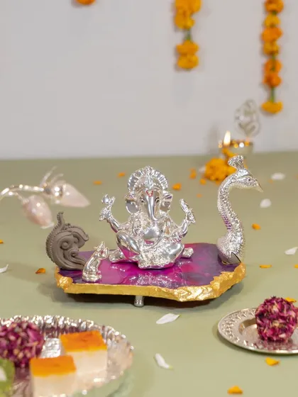 Lord Ganesha seated on a vibrant pink agate stone base, flanked by a peacock and his mouse. This colorful and artistic idol is a joyful celebration of faith, perfect for a modern home.